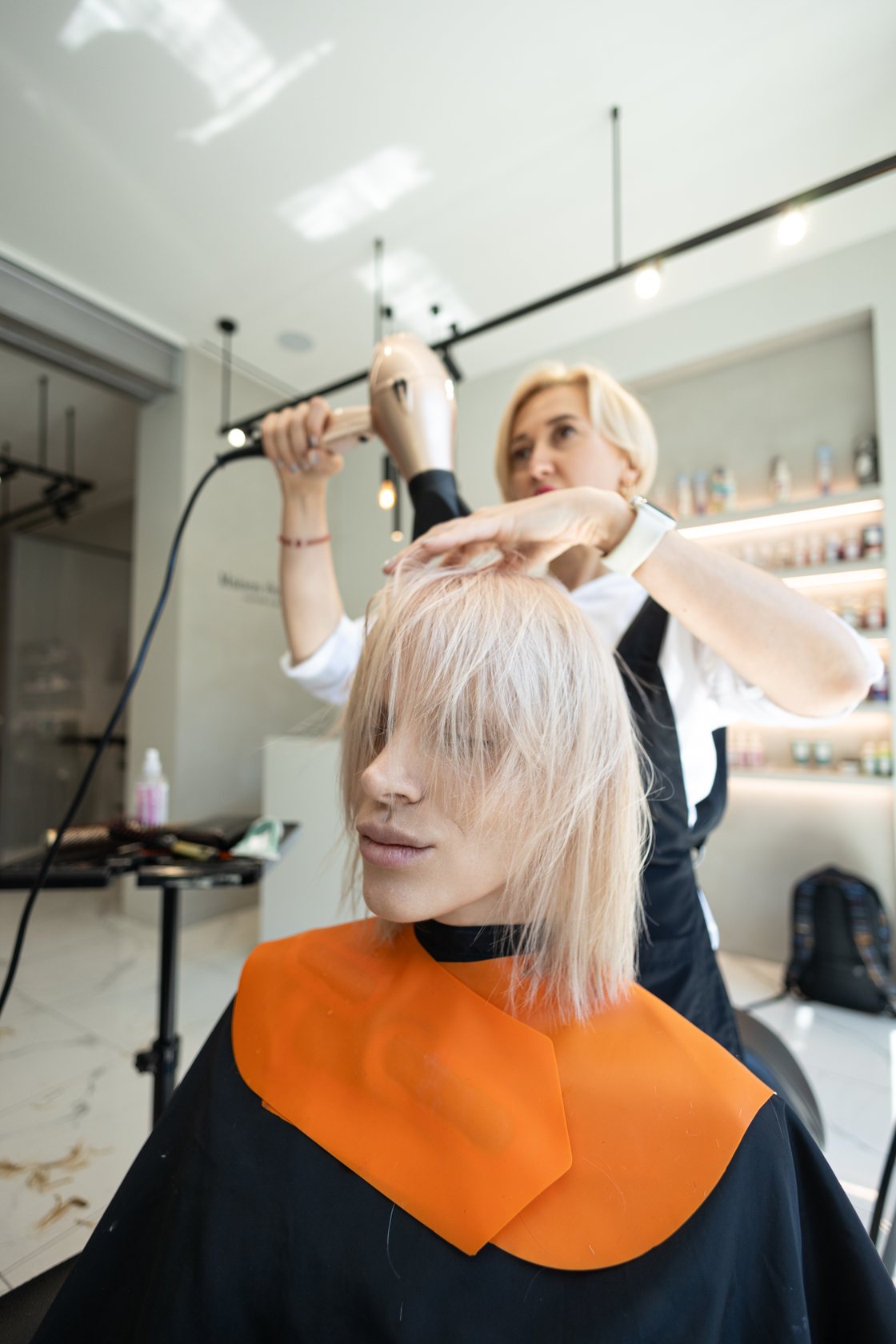 Stylist blow-drying a client's blonde bob in a bright Brussels salon