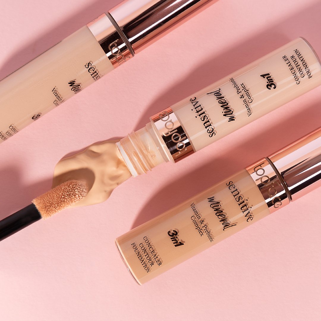 Three beige concealer tubes with rose-gold caps on pink, one applicator showing product
