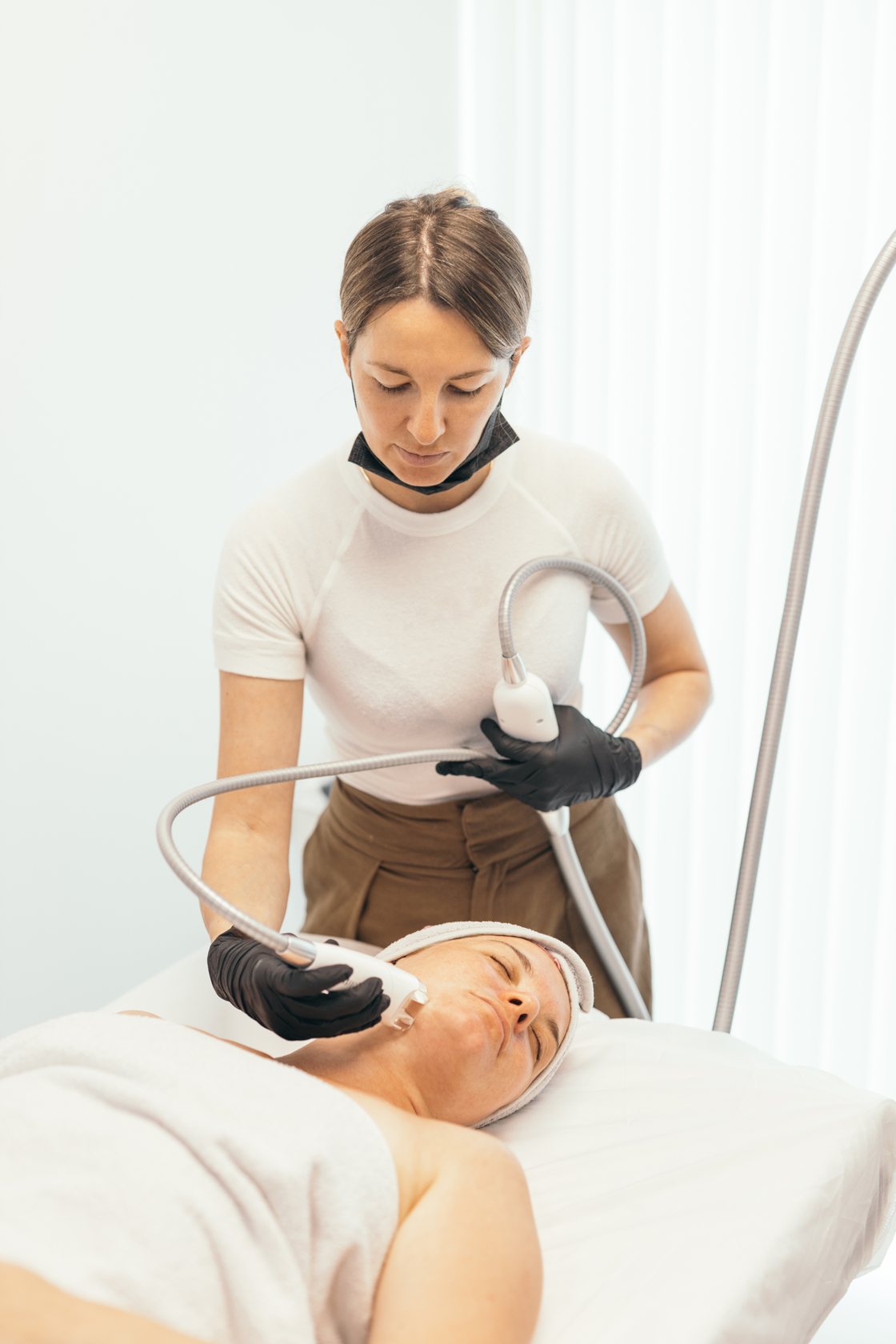 Therapist treating a client's face with a handheld device in a bright treatment room