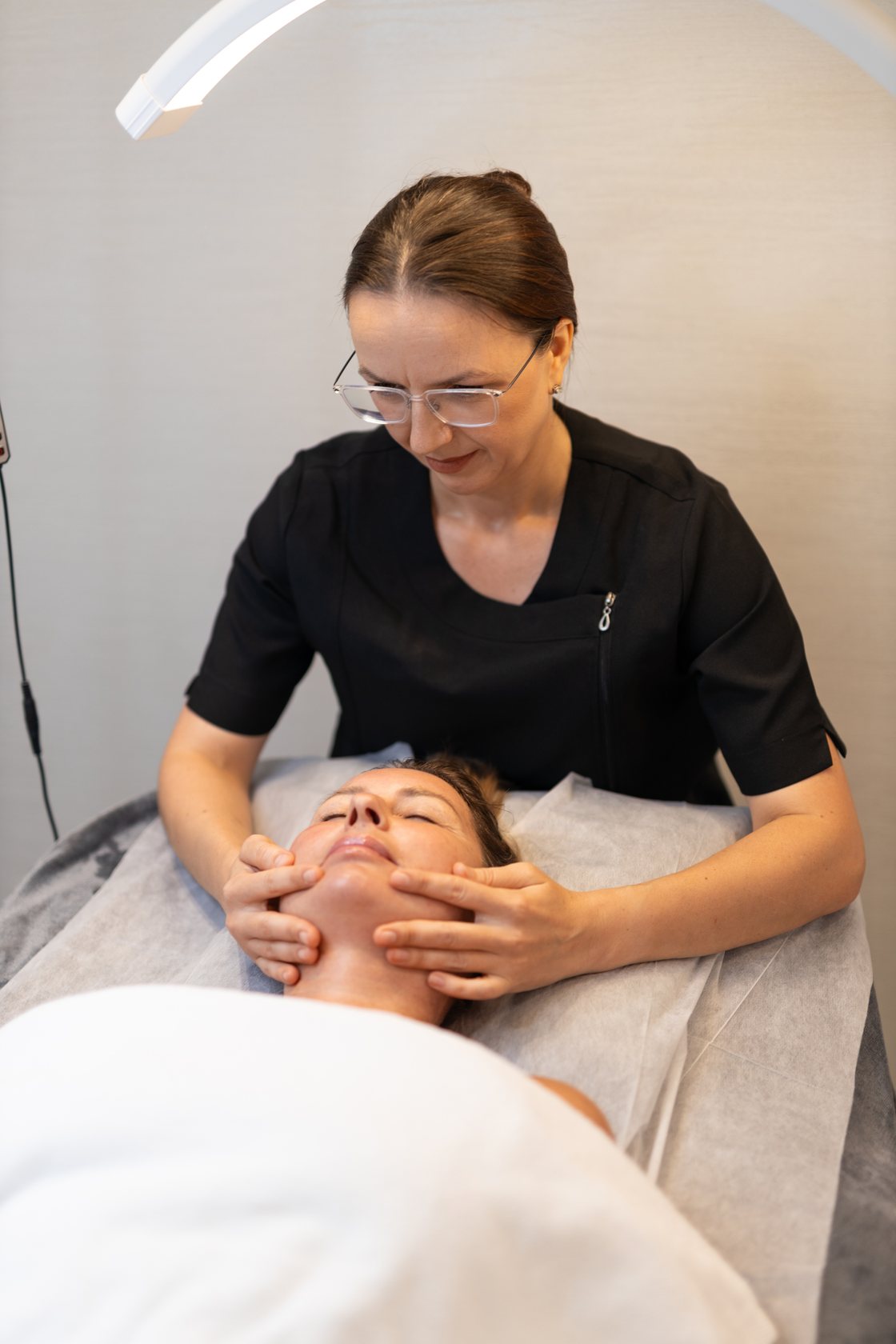 Esthetician giving a facial massage to a client lying on a treatment bed in a Brussels salon
