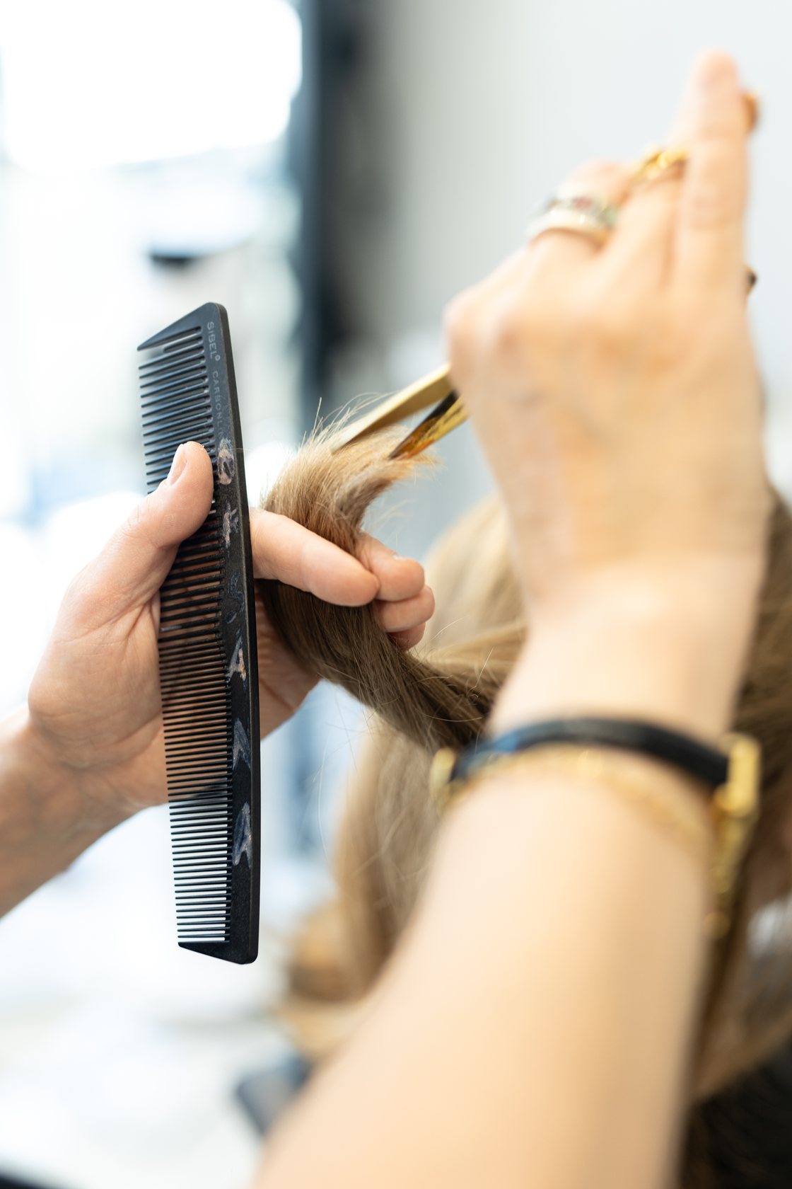 Close-up of a hairdresser's hands cutting a section of hair with scissors and a comb