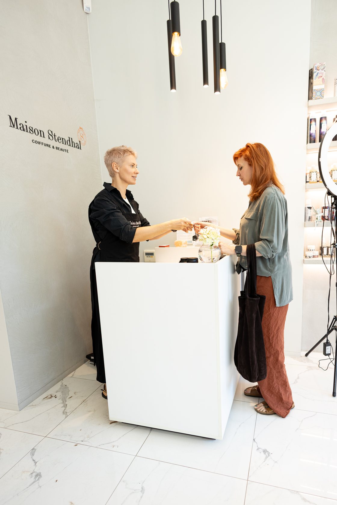 Stylist at the white reception desk handing an item to a client in a Brussels salon