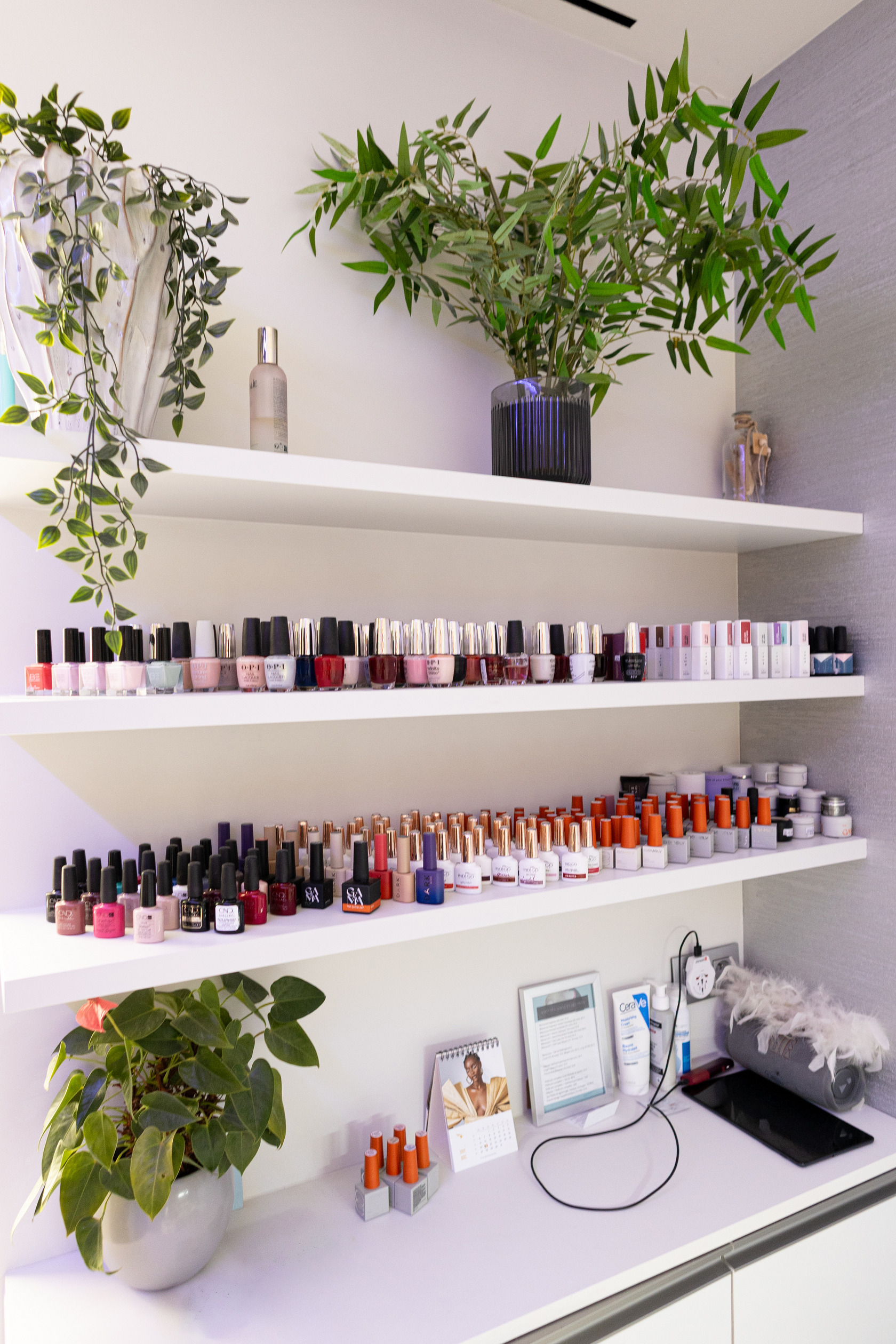 White shelves with rows of nail polish bottles and plants